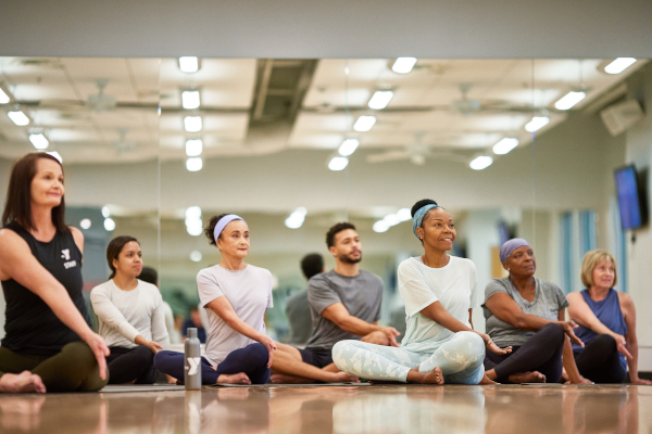 photo of seven people seated cross legged on the floor in a yoga pose that stretches the right arm over the left knee with the palm up.